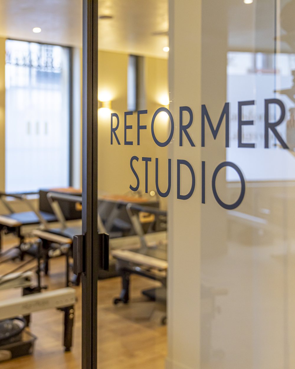 La porte vitrée du studio, lettrage REFORMER STUDIO, appliques et reformers en enfilade