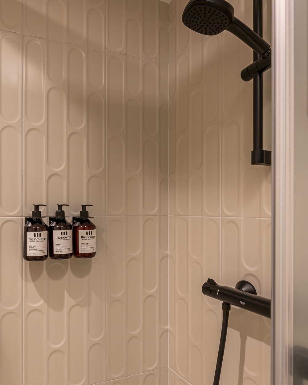 La douche : carreaux en relief, robinetterie noire, flacons The New Me